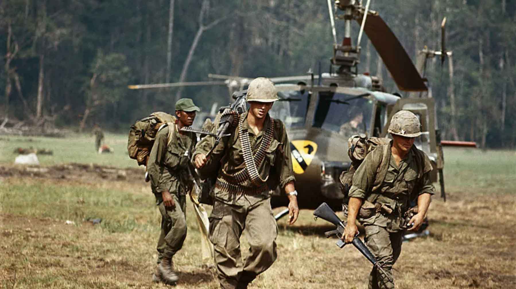 Soldiers from the Vietnam War carrying weapons in front of a helicopter