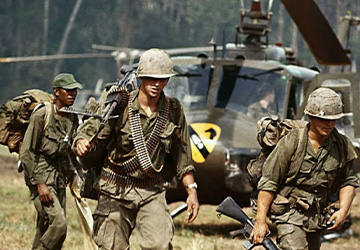Soldiers from the Vietnam War carrying weapons in front of a helicopter